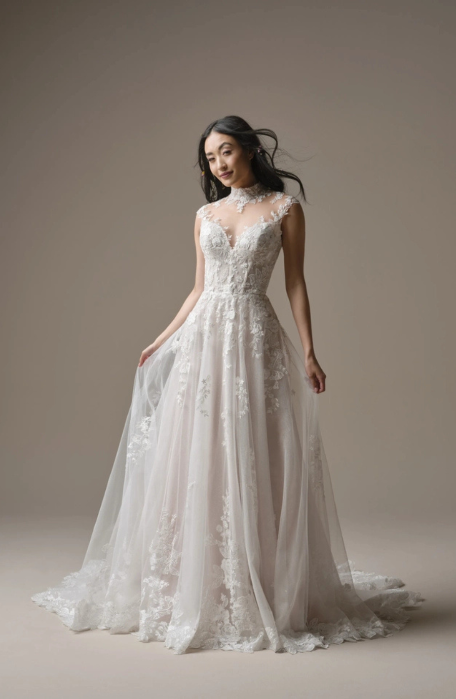A woman wearing a delicate, lace-trimmed wedding gown with a deep V-neckline, standing gracefully against a neutral background.