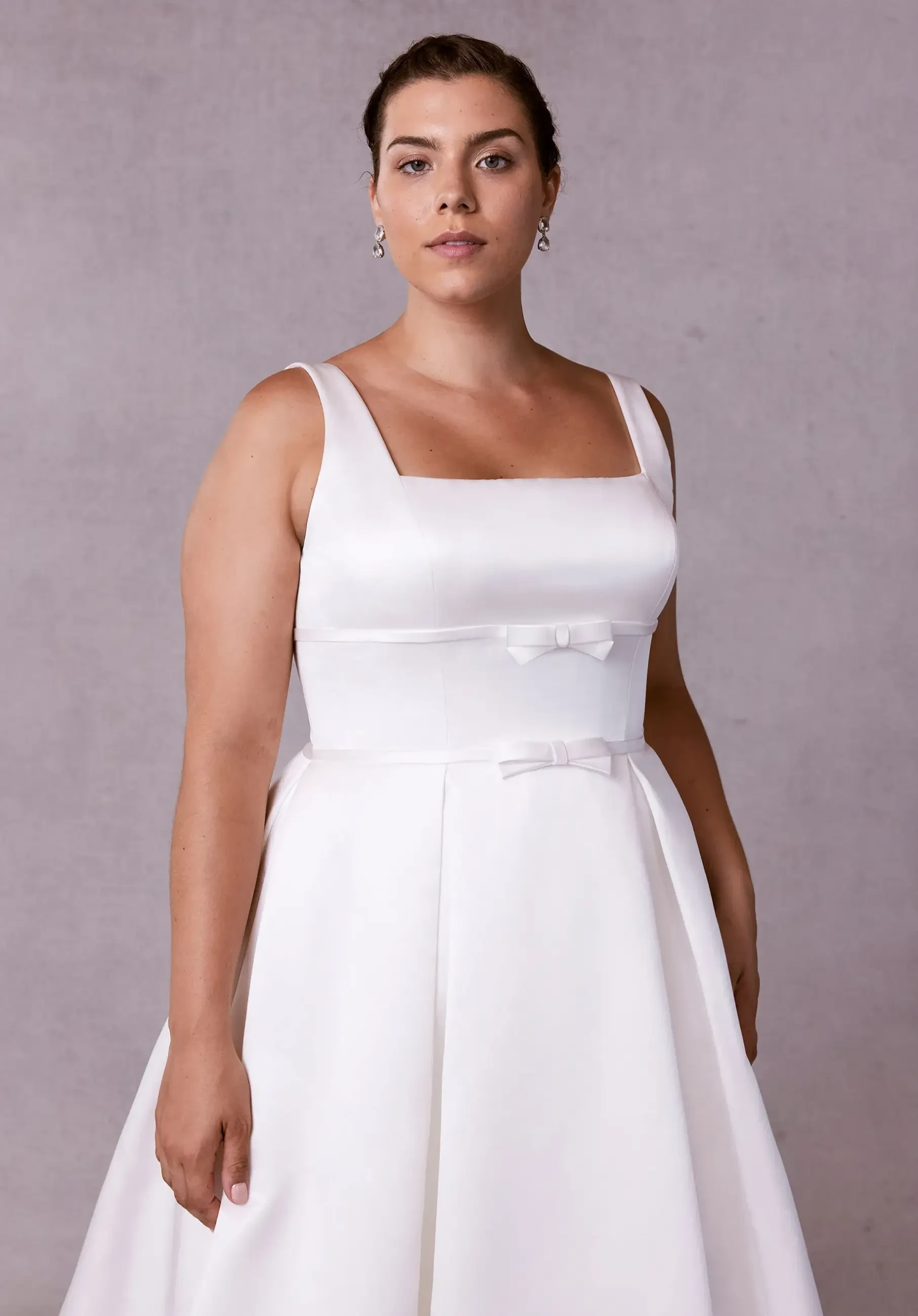 Model is wearing a sleeveless structured a-line wedding dress with a square neckline 
