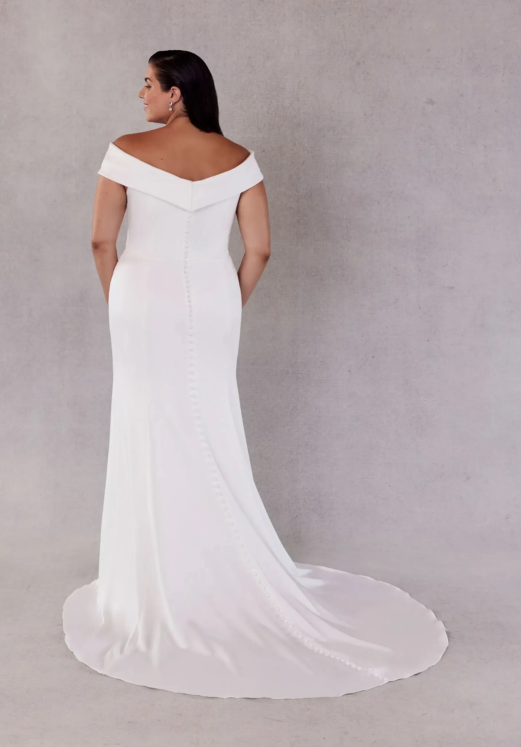 Model is wearing an off the shoulder plus size fit and flare wedding dress 
