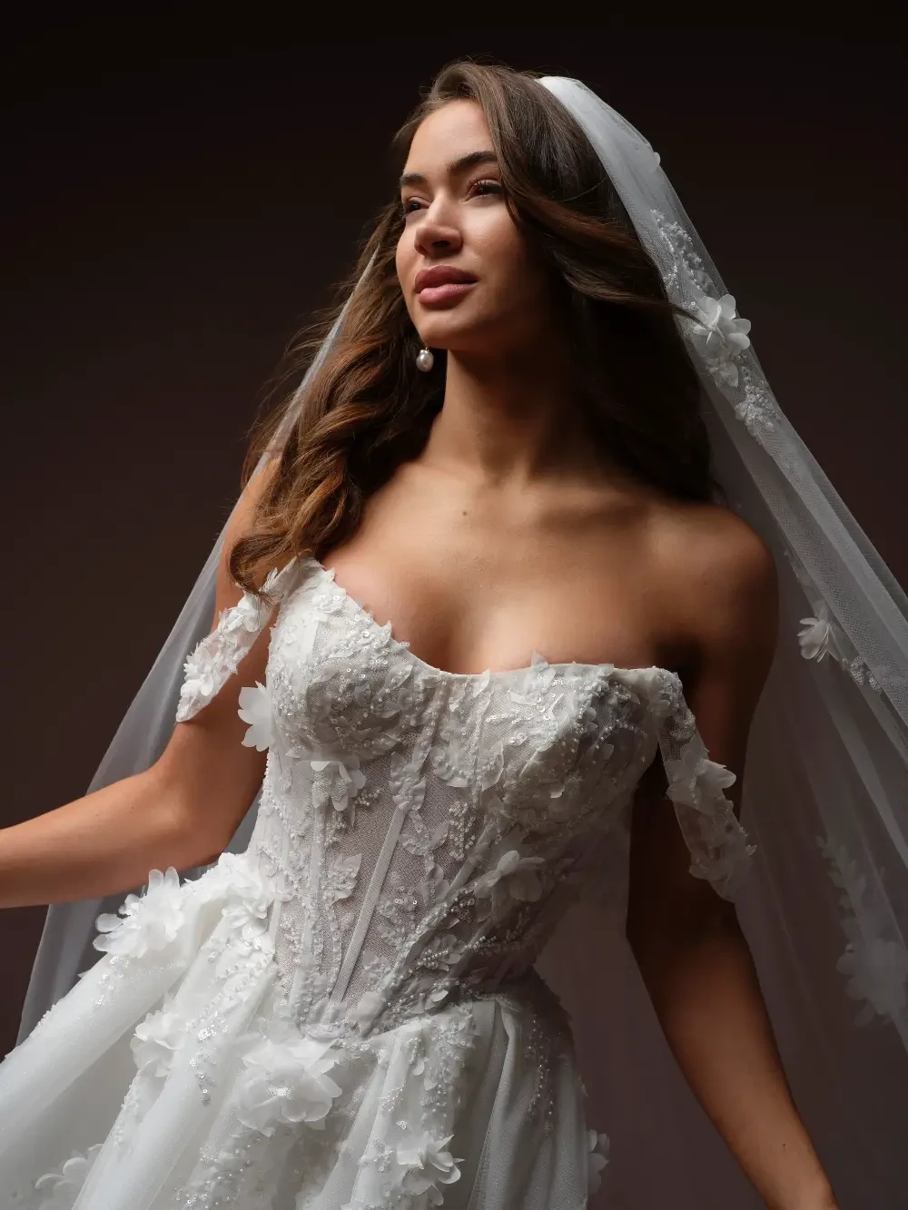 A woman in a stunning bridal gown, with intricate floral details, looking gracefully to the side while wearing a flowing veil.