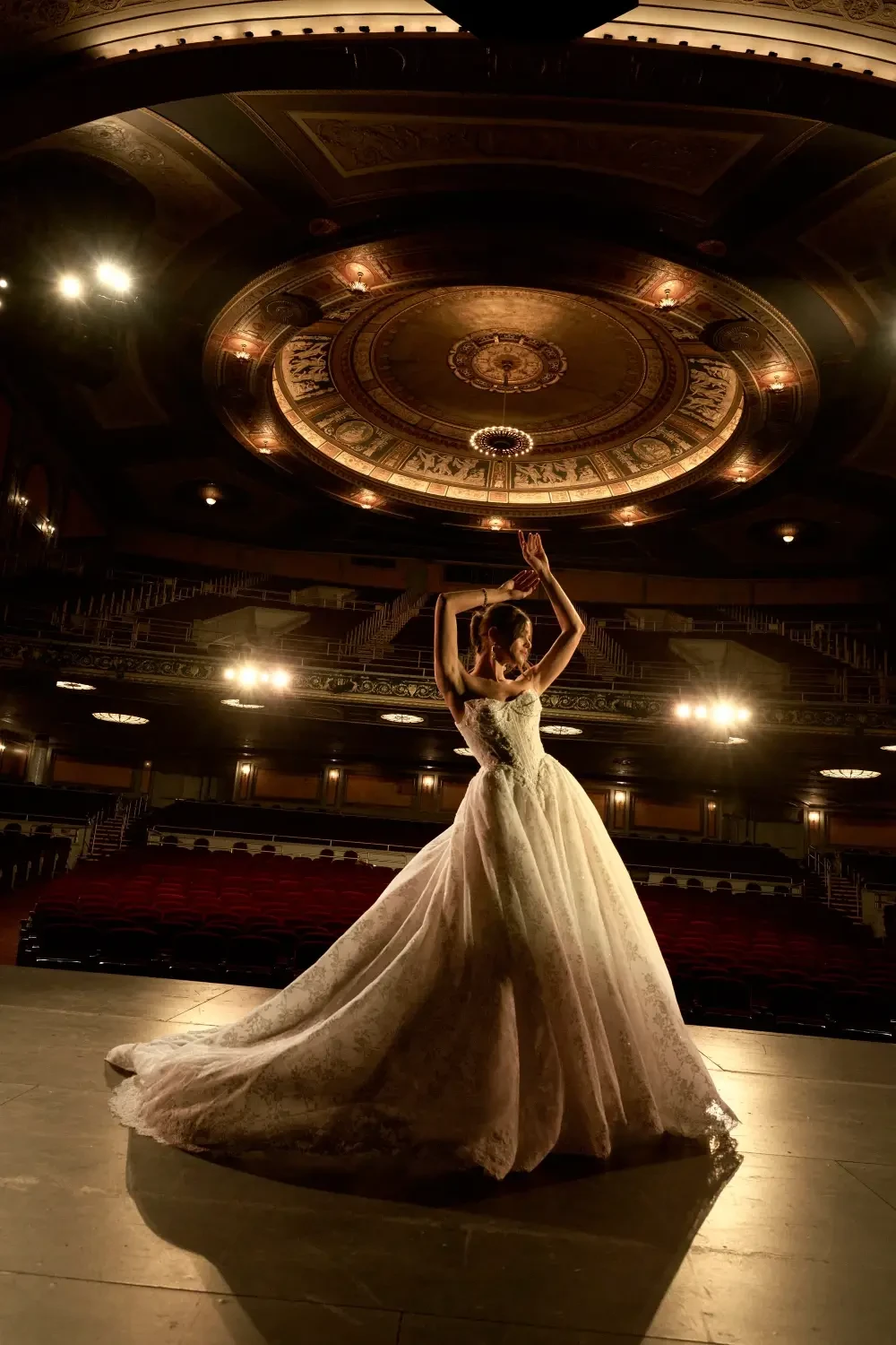 A bride in a flowing wedding gown poses gracefully on a stage in a beautifully lit theater.
