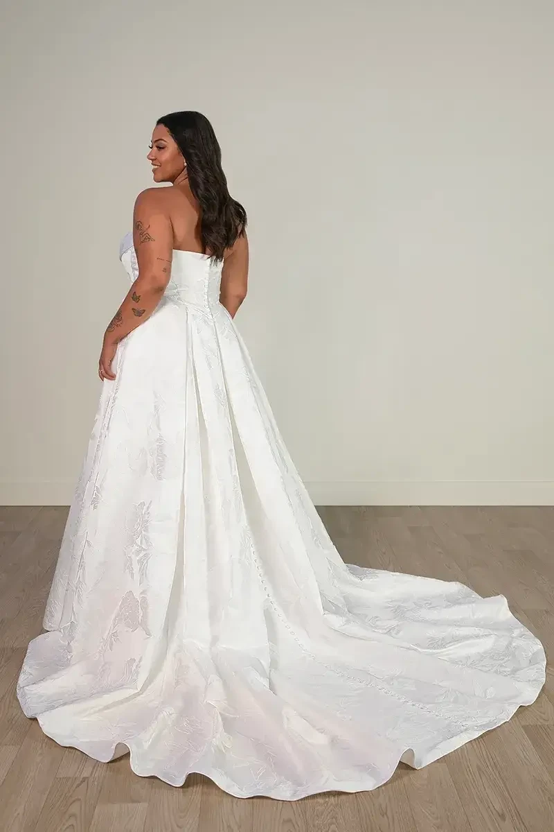Model is wearing a plus size strapless ball gown with a basque waist and ruched sweetheart neckline
