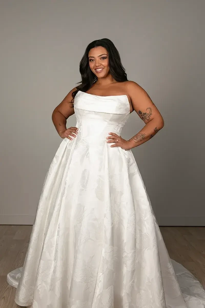 Model is wearing a plus size strapless ball gown with a basque waist and ruched sweetheart neckline